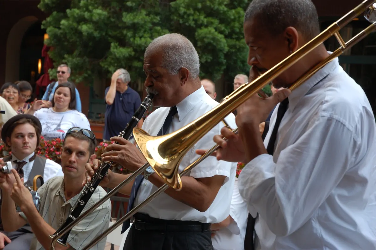 A clarinettist and a trombonist in white shirts and ties playing outdoors for a seated audience at a New Orleans traditional jazz concert