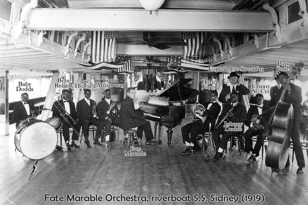 Black-and-white photograph of the Fate Marable Orchestra on the steamer Sidney in 1919: musicians in suits with drums, a grand piano, horns and a double bass under hanging flags